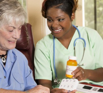 Caring, African descent home healthcare nurse conducts medical consultation with senior adult woman at her home or nursing home.  The female patient is sitting in her comfortable chair while reviewing her medications information with her nurse or doctor.  Backyard can be seen through the windows.